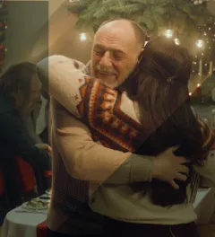 two people hugging with a Christmas scenario behind.